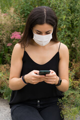 Young woman using a white face mark at a park checking her phone.