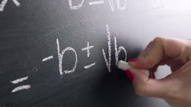 Math teacher writing equation or function on blackboard in school classroom. Student doing exercise on chalkboard in university or college. Woman teaching or studying. Close up with camera movement.