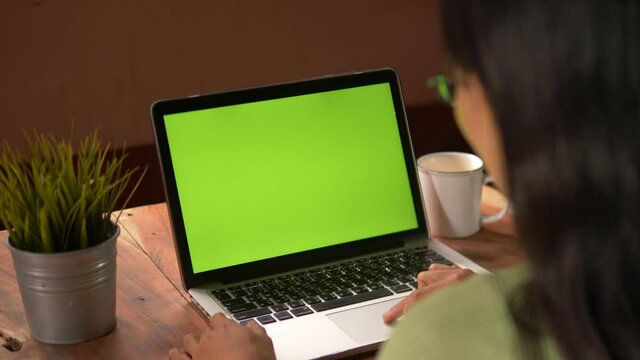 Side View of . Over the shoulder shot of a business woman working in office interior on pc on desk, looking at green screen. Office person using laptop computer with laptop green screen.