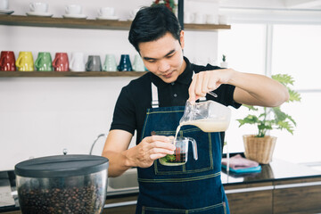 Barista man's hands are holding out a milk glass. Matcha green tea drink in a glass with milk. Useful latte. Cafe shop and business concept