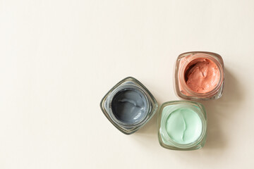 Facial clay mask on light beige background with copy space, top view. Pure green, pink and black clays. Skin care beauty detox product