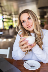 Portrait of young woman drinking coffee at table in cafe