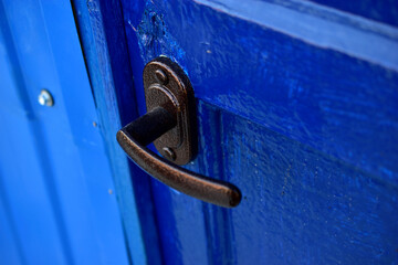 A brown iron handle on a freshly painted blue door