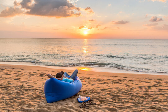 A young man enjoying the sunset over the Andaman sea lying on an inflatable sofa on an empty beach