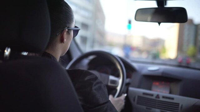 Woman driving car fast in city street with traffic. Road trip, speeding, escape or chase concept. Commuter, female taxi cab driver or ride share person. Interior back view of cockpit. Summer lifestyle