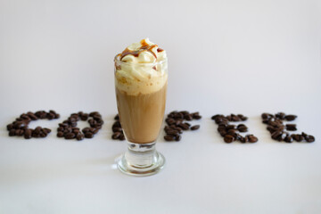 Iced coffee or Frappuccino with whipped cream and syrup .Coffee word on back, text made of roasted coffee beans isolated on white background.