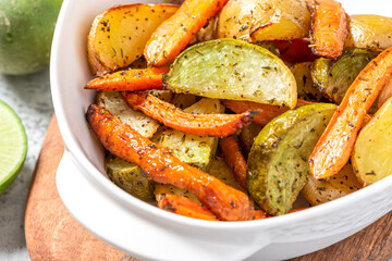 Baked vegetables in a white baking dish close-up. Fried potatoes, carrots and turnips with olive oil and herbs. Vegetarian food, autumn or winter food.