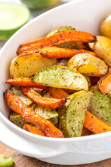 Baked vegetables in a white baking dish close-up. Fried potatoes, carrots and turnips with olive oil and herbs. Vegetarian food, autumn or winter food.