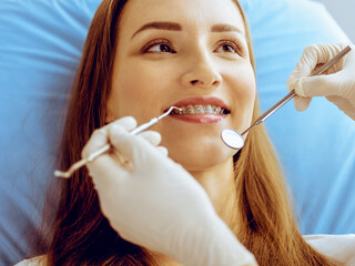 Smiling young woman with orthodontic brackets examined by dentist in dental clinic. Healthy teeth...