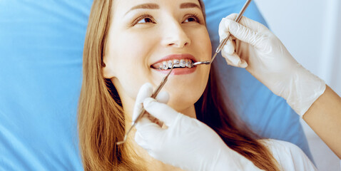 Smiling young woman with orthodontic brackets examined by dentist in dental clinic. Healthy teeth and medical care concept