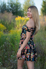 Naklejka na ściany i meble overlight bright portrait of a charming attractive blonde in flowery dress in the field. 