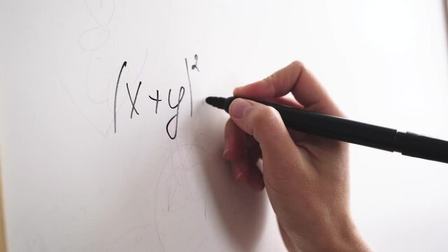 Female hand writes a formula with a marker on a white board