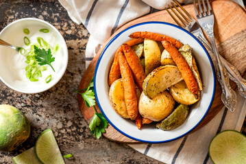 Baked vegetables. Roasted potatoes, carrots and radish with herbs in a bowl on a dark background top view. Vegetarian food, rustic style.