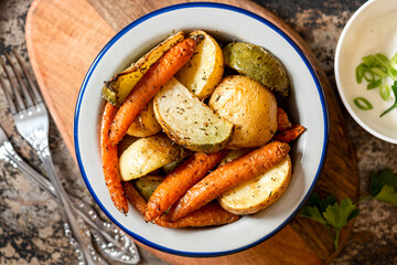 Baked vegetables. Roasted potatoes, carrots and radish with herbs in a bowl on a dark background top view. Vegetarian food, rustic style.