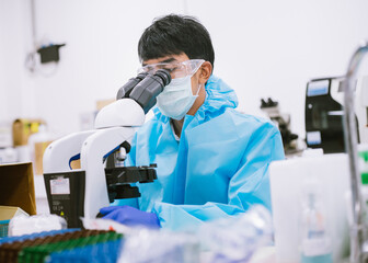Scientist in protection suit and masks using microscope in research laboratory