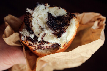 Poppy seed bun in the hand of a man on a dark background, close-up