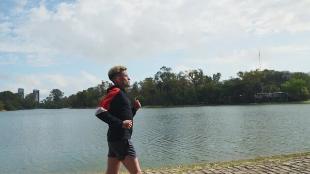 Profile shot following a handsome man running beside lake. Slow motion. High quality FullHD footage