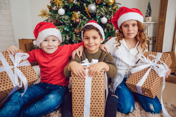 Children with gifts are sitting near the Christmas tree. New Year.