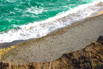 Beach and turquoise sea with waves near the sand. View from above