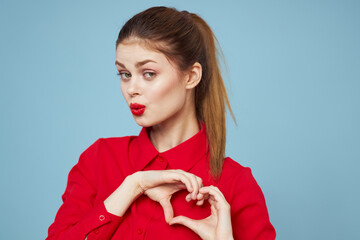 A girl in bright clothes shows a heart with her hands on a blue background cropped view