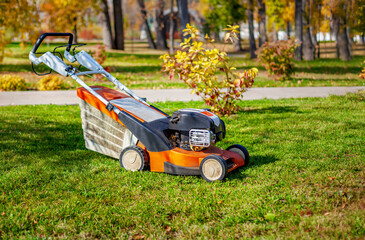 Lawn mower machine on green grass in autumn park.