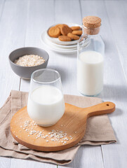 a glass and bottle of vegan milk with oatmeal cookies on a white wooden background