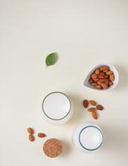 Obraz na płótnie Canvas a glass and bottle of fresh vegan almond milk and a few scattered nuts on a light background.