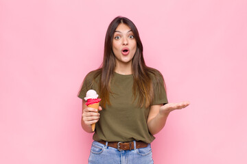 young pretty woman with an ice cream feeling extremely shocked and surprised, anxious and...
