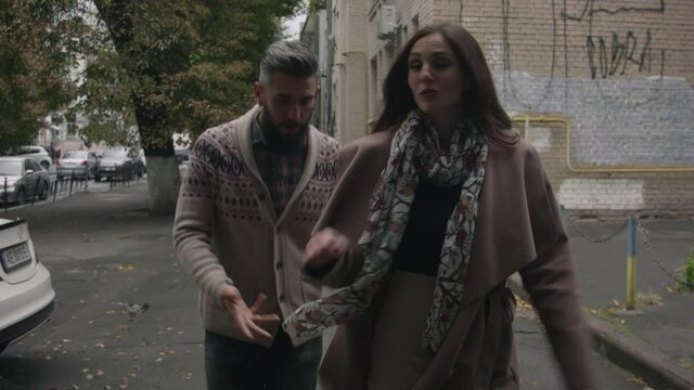 Middle-aged man and woman cursing on a city street in autumn on a cloudy day. A man in a sweater and a woman in a coat argue on the streets of the city and sort things out.