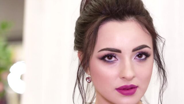 Brunette girl with beautiful makeup and hairstyle posing in front of the camera in a purple dress. Video