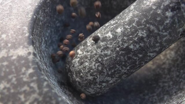 Super close-up of black peppercorns falling into the grey stone mortar in slow motion