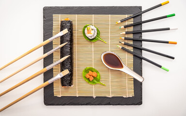 Présentation de plat de cuisine Japonaise, sushi et maki sur fond noir avec pinceaux et crayons de couleurs en décoration.	