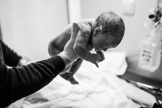 Newborn child seconds and minutes after birth. Doctor hands with new born baby. Medical check up of health and reflexes of child. New life, beginning, healthcare