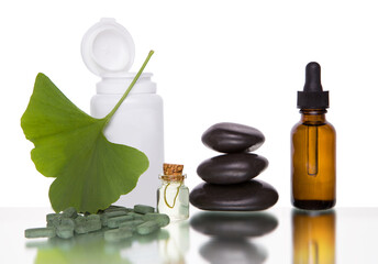 Pills with extract from the ginkgo in bottle and green leaves isolated on a white background.