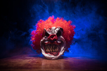 Spooky Clown head on wooden table. Evil clown head smiling on dark foggy background. Halloween...
