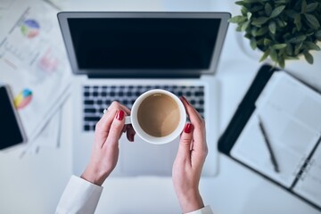 Top view image of woman holding coffee in the office desk over the laptop.