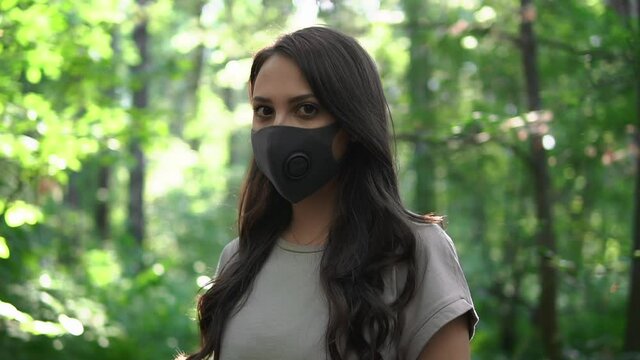 Portrait Of Young Woman Wearing Respiratory Face Mask In Park During Global Epidemic Of Covid-19 Coronavirus, Modern Respirator For Air Purification And Protection From Airborne Bacteria And Viruses