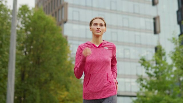 Medium shot of athletic young woman running down city street during daily jogging workout
