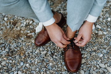 Happy groom tied the laces on the shoes close up. Man is hanging shoes outdoor on the stone background. mans hands and pair of leather men's shoes. Getting ready wedding concept.
