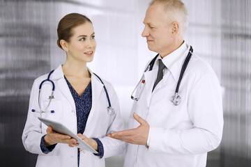 Elderly confident doctor and woman physician discussing current disease therapy while standing in...