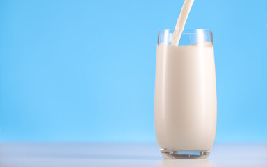 Glass of milk on a white table and blue background. Pouring milk into glass. Organic milk product.
