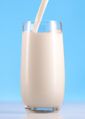 Glass of milk on a white table and blue background. Pouring milk into glass. Organic milk product.