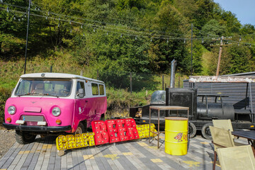 Naklejka premium Kvasy, Zakarpattia region, Ukraine. September 20, 2020. Part of the beer zone of Hutsul craft brewery. Vintage cars, pink UAZ 452, and a black locomotive. Illumination inscriptions.
