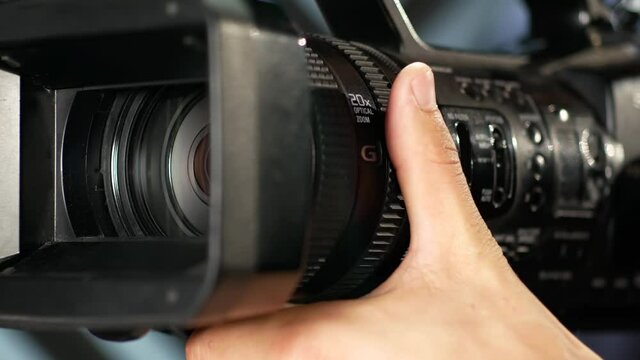 Сlose-up of the videographer's hand as it turns the zoom ring, turns on the ND filter, and adjusts the aperture value. The videographer focuses and adjusts the video camera in the studio before filmin