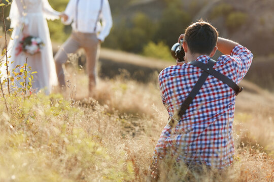 wedding professional photographer takes pictures of wedding couple in nature on the sunset, man photographer in action
