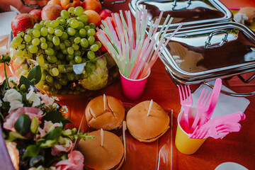 Birthday table with hamburgers, grape, flowers, plastic cups and straws.