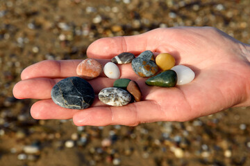 close-up of female hands holding colorful beach rocks with blurred beach background.