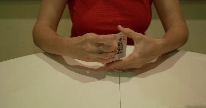 Woman in red shirt shuffling a deck of cards on a white table