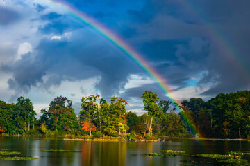 Beautiful half rainbow over an island and lake with trees in morning light with storm clouds near Oak Grove, Michigan, USA in early autumn 