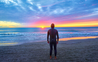 Young athlete swimmer on the beach with a nice sunrise of very colorful clouds